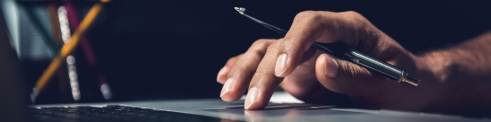 Person with pen in hand typing on computer